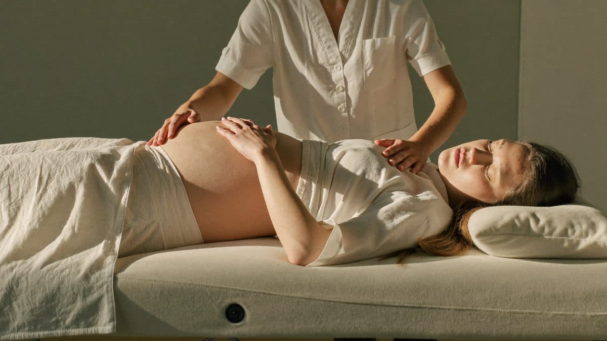 Femme enceinte détendue sur une table de massage, mains de la praticienne posées sur ses jambes